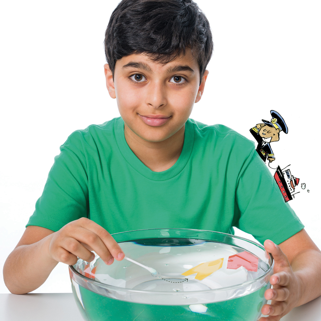 Un jeune devant un grand bol d'eau qui fais avancer un bateau en papier avec un coton-tige et du savon à vaisselle